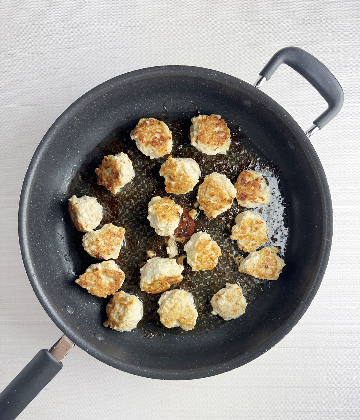 Browned chicken meatballs in a skillet.