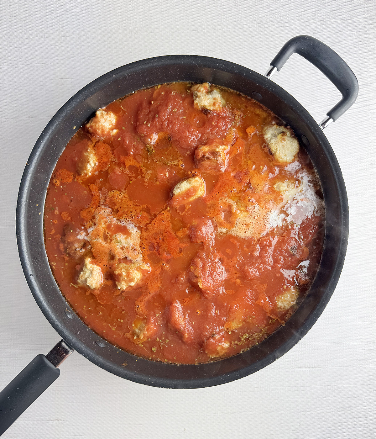 Chicken parmesan meatballs cooking in sauce.