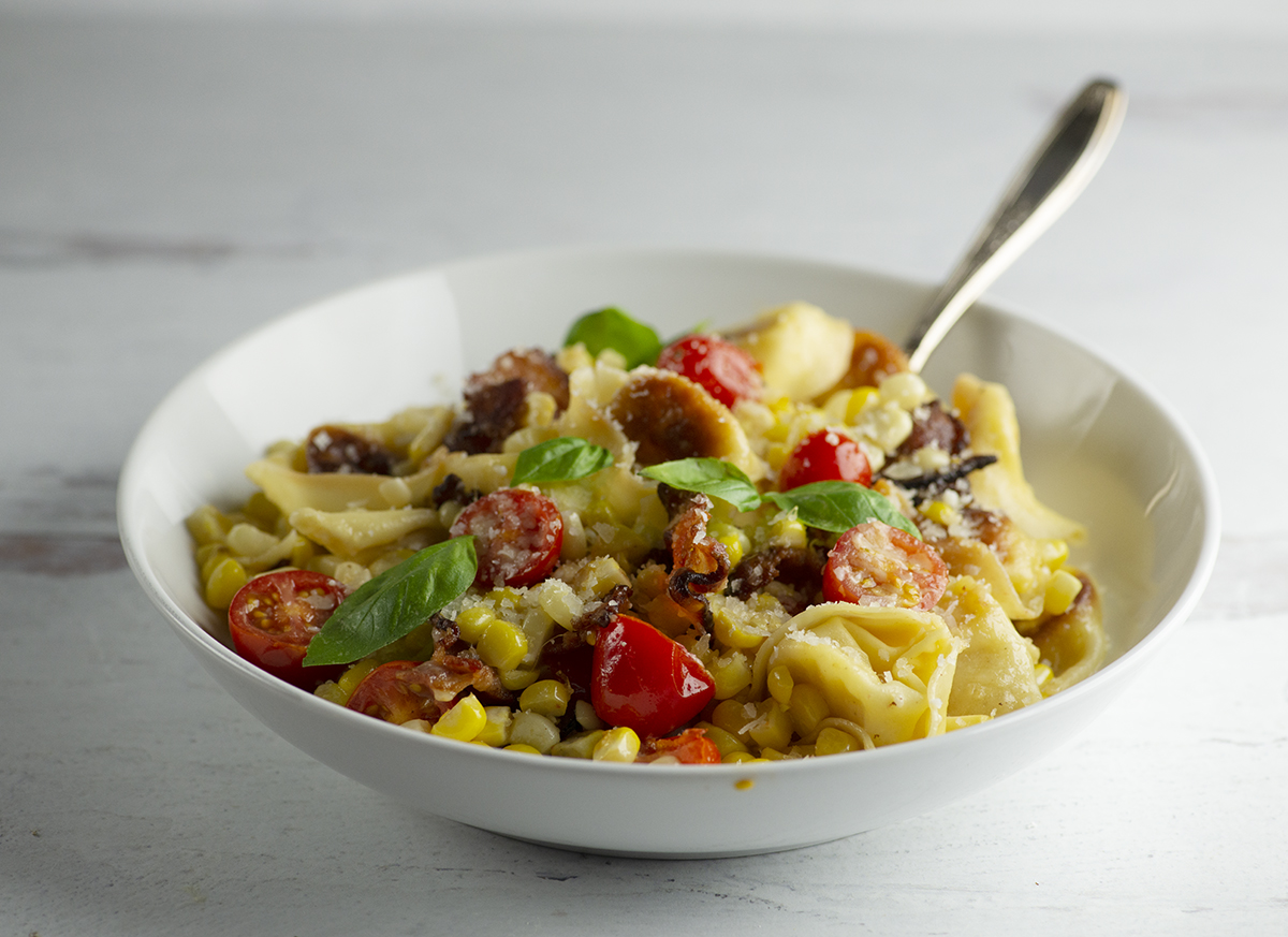 Pan Fried Tortellini with Bacon Tomatoes and Corn in a bowl with a fork.