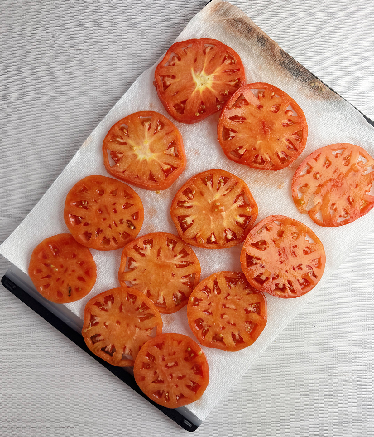 Sliced tomatoes draining on paper towels.