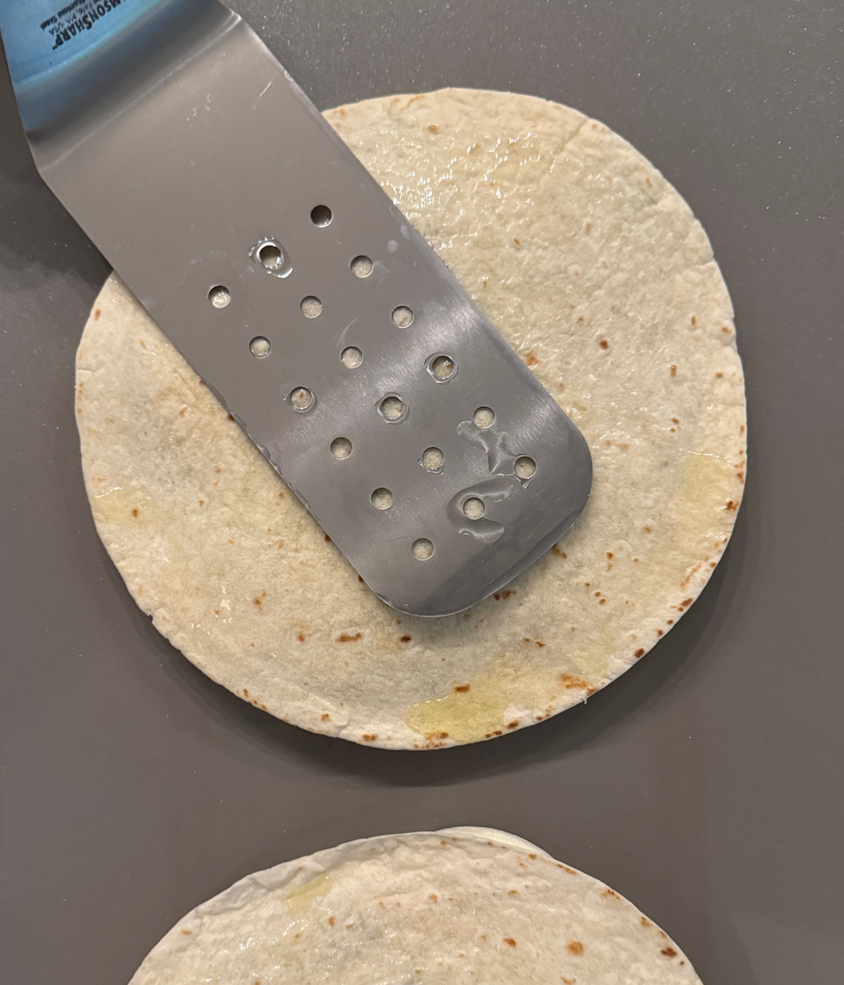 Spatula pressing caprese quesadilla on the griddle.