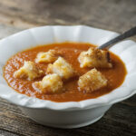 Tomato soup with grilled cheese croutons in a bowl.