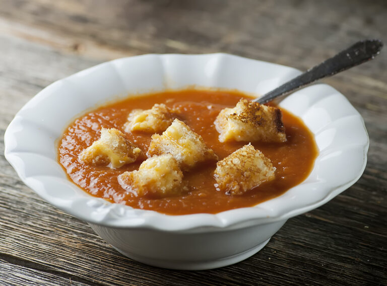 Tomato soup with grilled cheese croutons in a bowl.