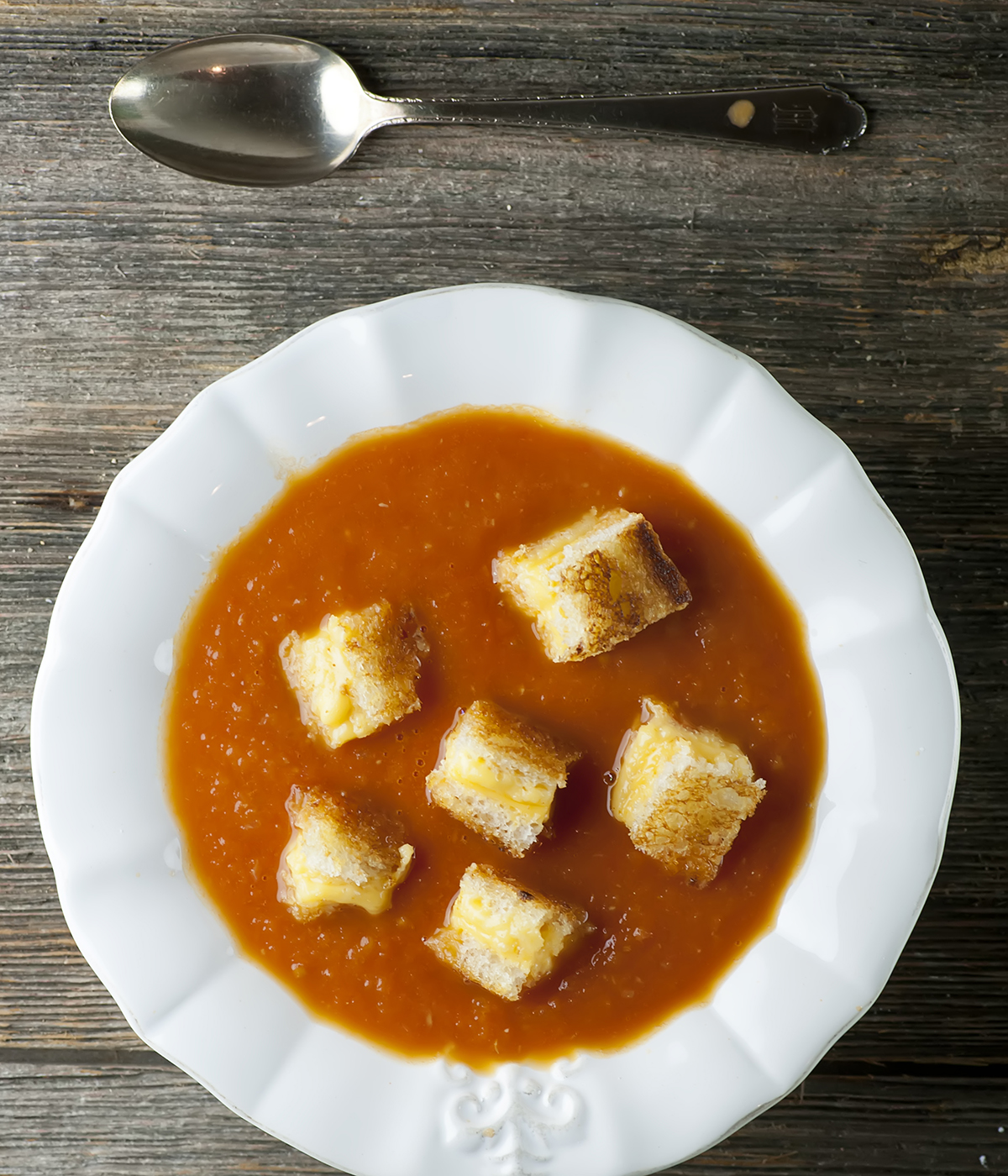 Tomato soup with grilled cheese croutons in a bowl with a spoon.