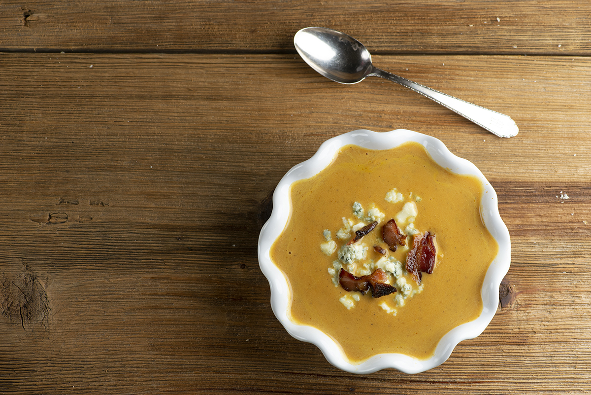 Pumpkin Bacon Soup In A Bowl on a wooden counter.