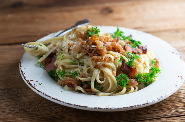 Pasta with bacon bread crumb sauce on a plate with a fork.
