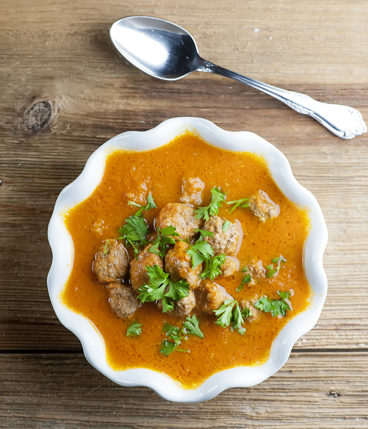 Tomato meatball soup in a bowl with a spoon.