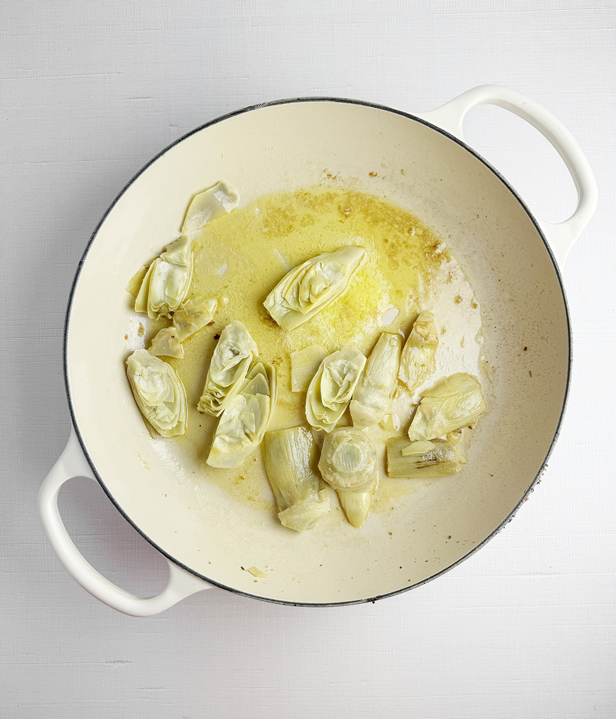 Artichokes in a butter sauce in a skillet.