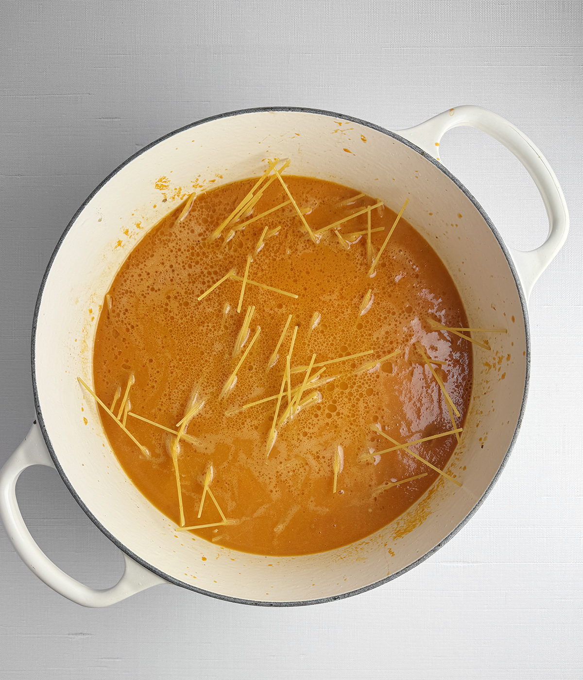 Spaghetti cooking in tomato sauce in a pot.