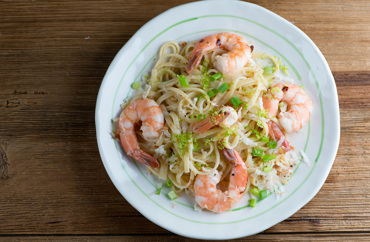Toasted coconut shrimp pasta on a wooden counter.