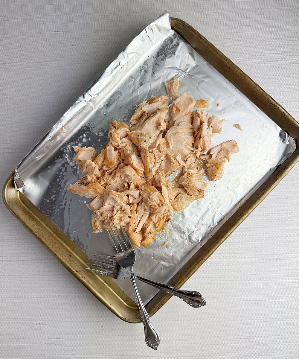 Shredded salmon with two forks on a baking sheet.